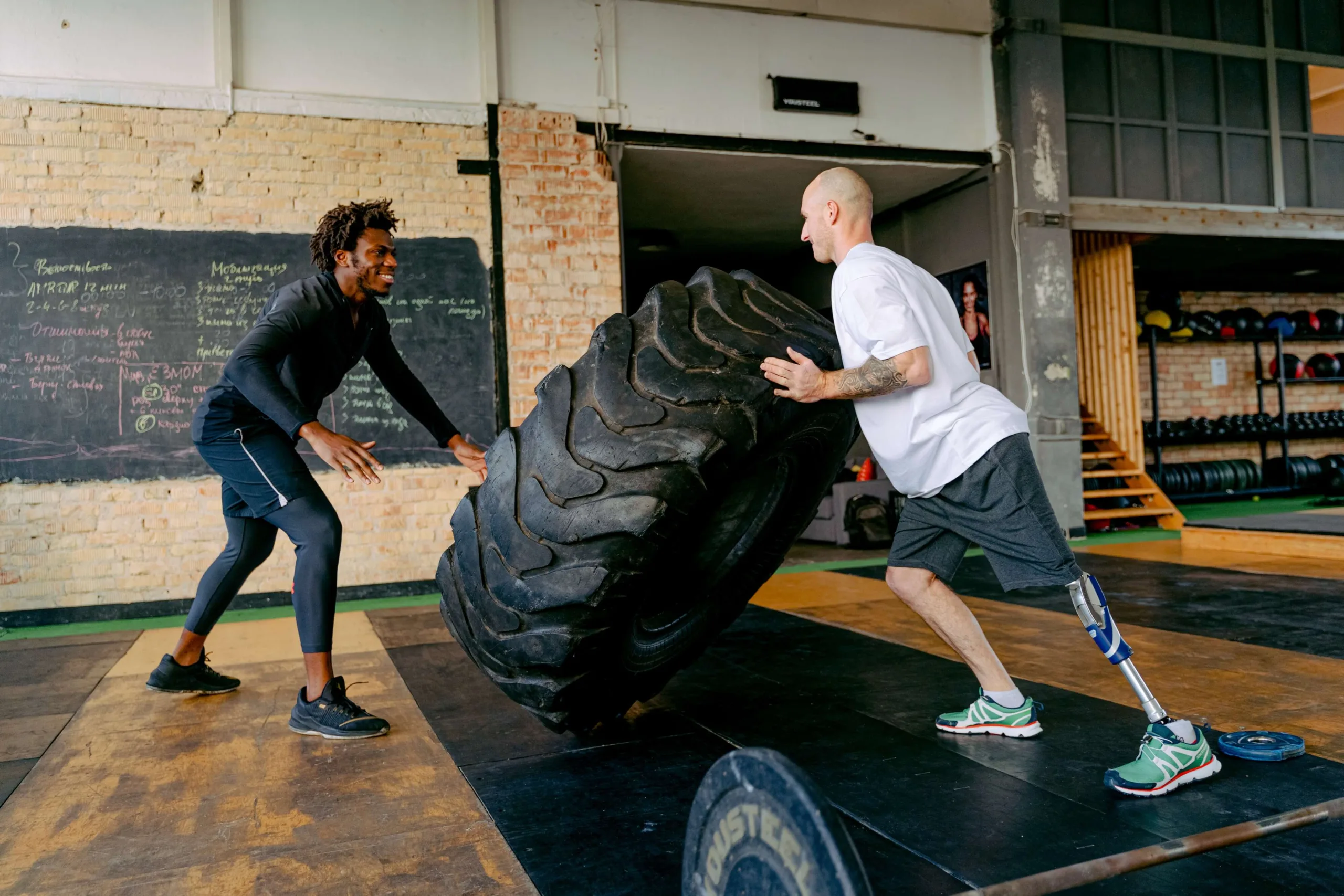 a personal trainer encouraging his client who has a prosthetic leg to lift a tire